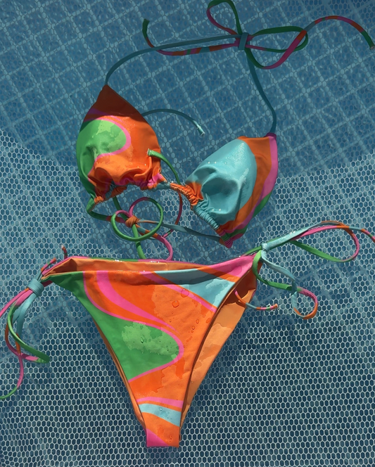 Colorful bikini set on a textured surface with a pink and white striped fabric in the background.